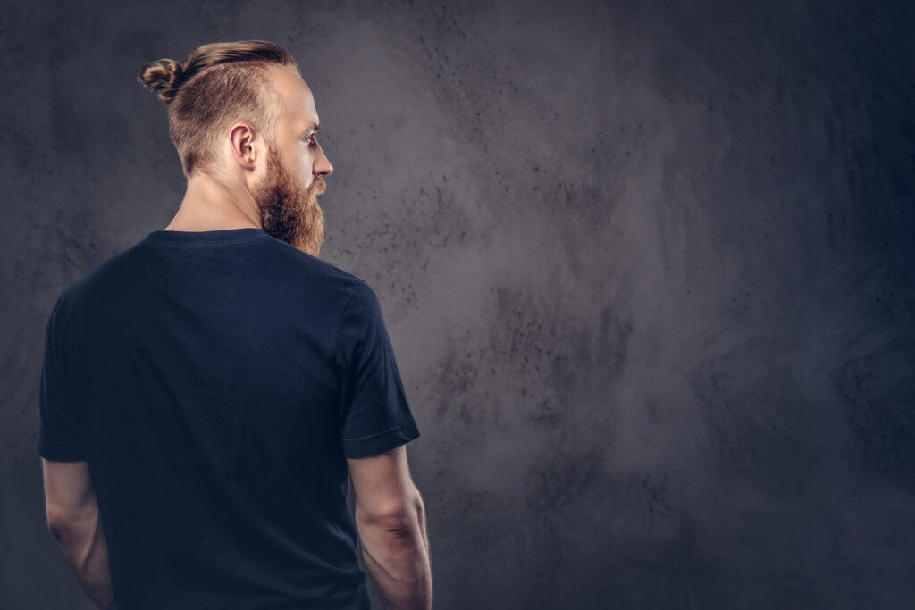 Back view of a redhead bearded man dressed in a black t-shirt. Isolated on a dark textured background.